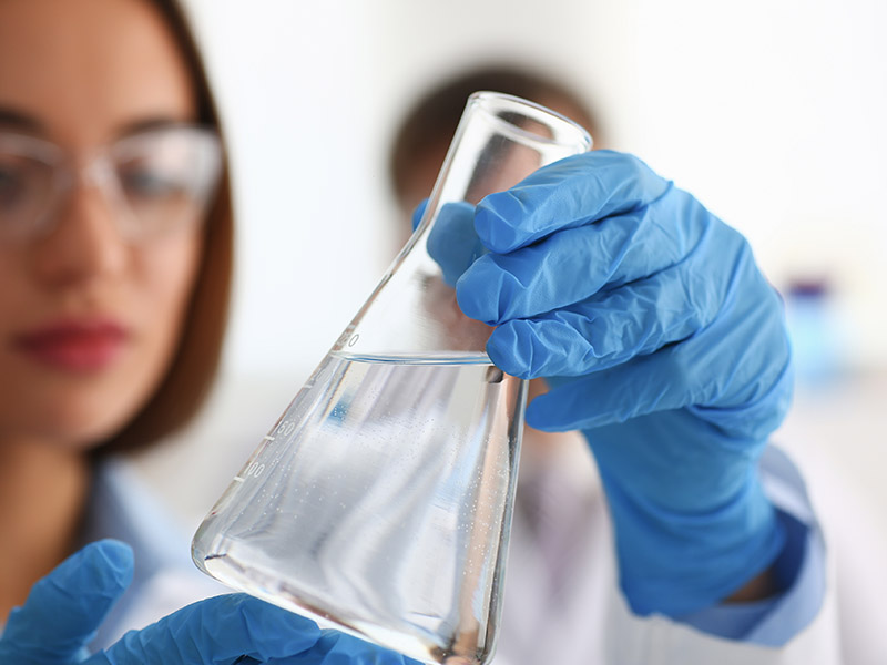 Laboratory technician observing water in a beaker for testing.