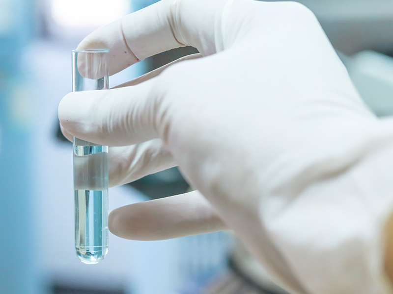 Test tube filled with water being held in a gloved hand.