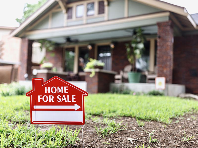"For Sale" sign in front of a single-family home