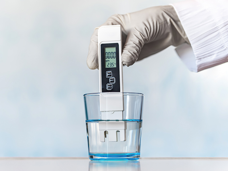 Water quality expert using a testing tool to check pH levels in glass of water.